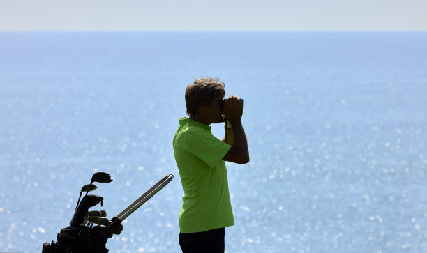 高尔夫球手在高尔夫球场上用激光测距仪精确地测量到旗子的距离。背景是海洋。大加那利岛图片下载