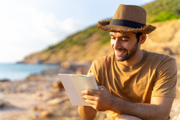 白人男子坐在海岸线山上写下旅行回忆。图片下载