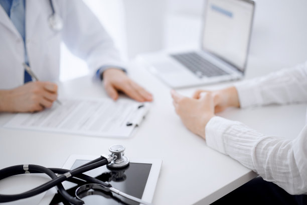 听诊器放在平板电脑上，医生和病人面对面坐在后面。医学、保健概念图片下载