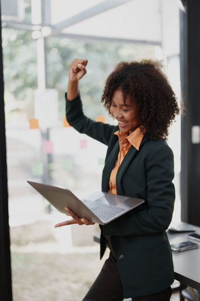 美丽的年轻少年美国非洲裔商业妇女手持电脑笔记本电脑，双手在获胜者是手势，高兴地庆祝成功的成就成功图片下载