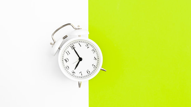 白色闹钟在白色和绿色的背景，平铺。图片下载