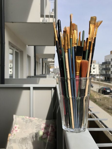 在阳台的边缘，以城市庭院为背景，一个透明的玻璃里摆放着许多艺术家的画笔图片下载