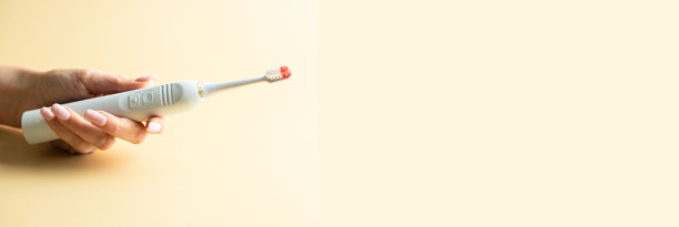 米色背景的女性手握电动牙刷。牙科护理休息室，带有复制空间的横幅图片下载