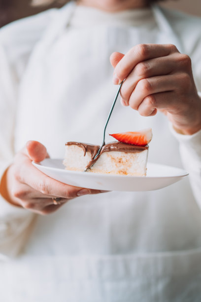 身穿白色制服的糖果师拿着一个盘子，里面有一块蛋糕和一把勺子图片下载