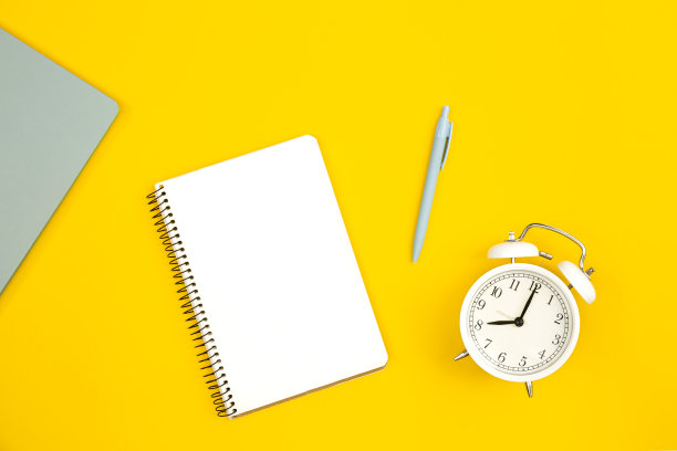 白色闹钟和黄色背景的空白记事本，平铺。图片下载