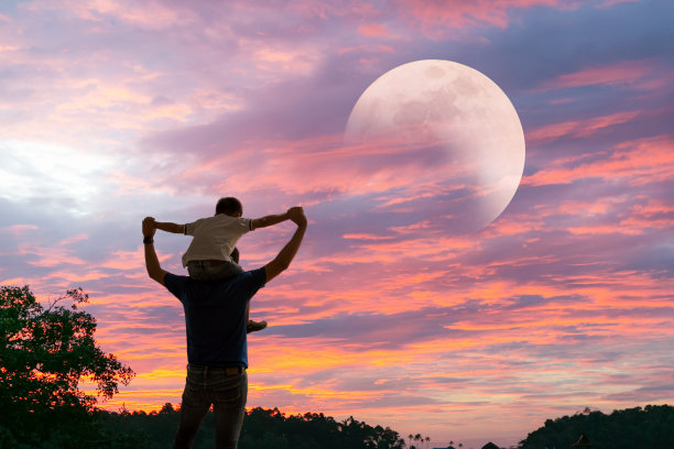 快乐的爸爸把儿子扛在肩上，和月亮一起展望未来的项目。父子的剪影。图片下载