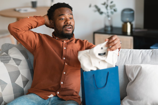 惊讶的黑人男子打开购物袋与新衣服在室内图片下载
