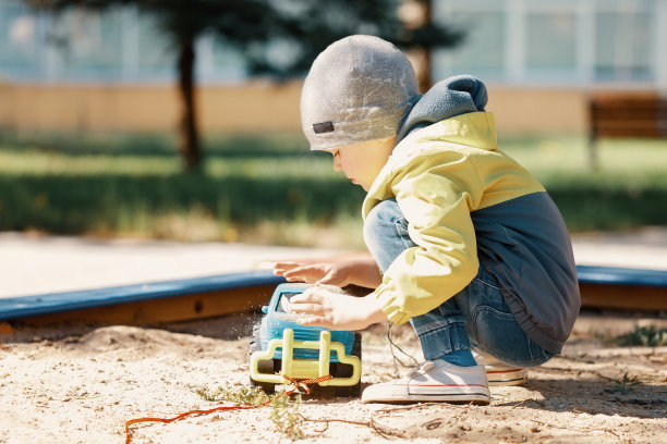 一个小男孩在户外操场上玩沙箱。蹒跚学步的孩子玩玩具车和装载沙子。适合孩子的户外创意活动图片下载