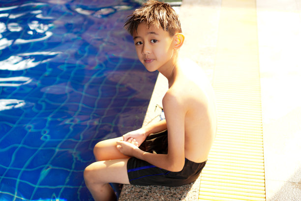 图为一个孩子坐在泳池边热身，准备去游泳。图片下载