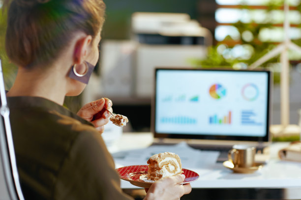 从后面看，一个现代女人拿着笔记本电脑和一块蛋糕图片下载