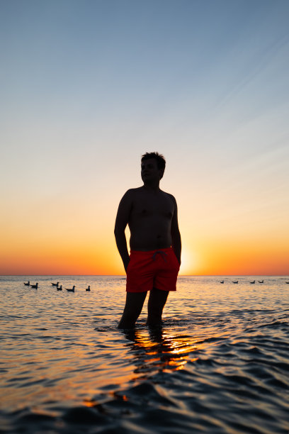 男性男性的剪影，漂浮的海鸥剪影在海水上黄蓝色的日落天空。垂直照片，选择性对焦图片下载
