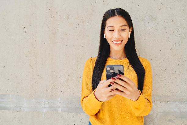 快乐的亚洲妇女的肖像使用智能手机站在城市的混凝土墙图片下载