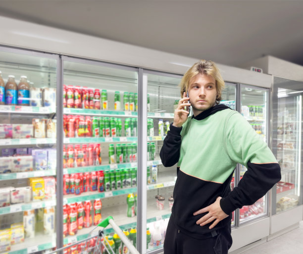 一名男子从超市冰柜中挑选冷冻食品。，阅读产品信息图片下载