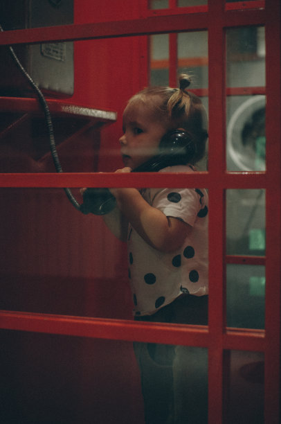 可爱的小女孩在一个红色的传统电话亭。小女孩手里拿着一部旧电话的听筒，惊讶地听着。一个红色的旧电话亭，里面有一个小孩。图片下载