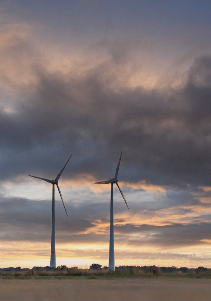 日落时的风力涡轮机农场。多云的背景图片下载