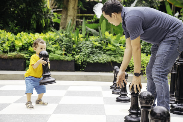 一位亚洲父亲和他的孩子在公园里下巨型国际象棋图片下载