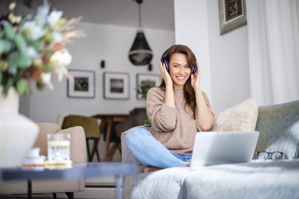 开朗的女人使用耳机和笔记本电脑，在家里放松图片下载