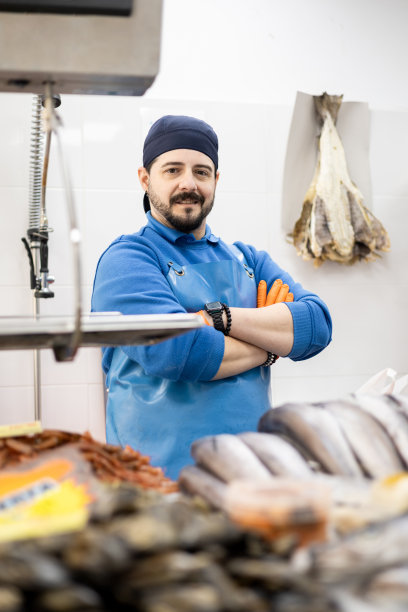 垂直的照片。一位中年鱼贩在销售柜台后双手交叉摆姿势，出售食品，中小企业经营理念。图片下载