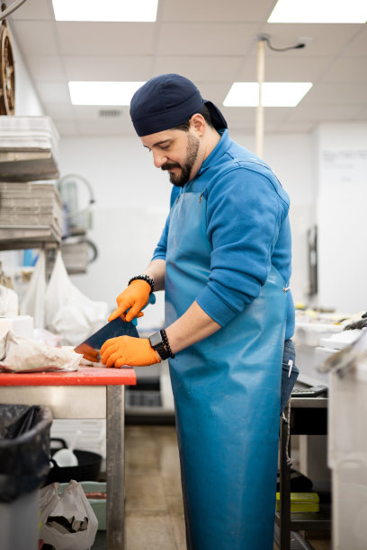 垂直的照片。一名中年鱼贩正在用月牙刀在砧板上切鱼，卖给顾客，这是一种中小企业经营理念。图片下载