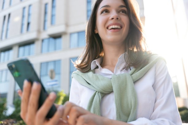 年轻的商业女性穿着专业的外表微笑着自信地使用智能手机在城市。图片下载