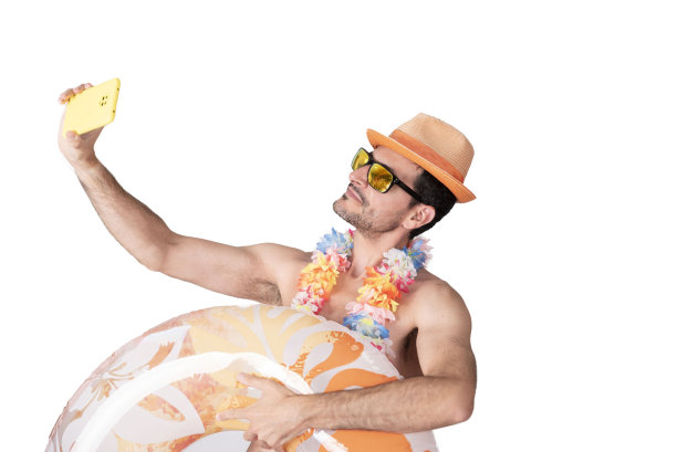 一名年轻男性游客戴着花项链、帽子和太阳镜，举着充气浮筒摆姿势自拍。图片下载