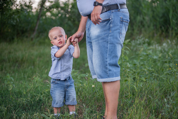 儿子握着父亲的手，看着镜头的照片。儿童保护日图片下载