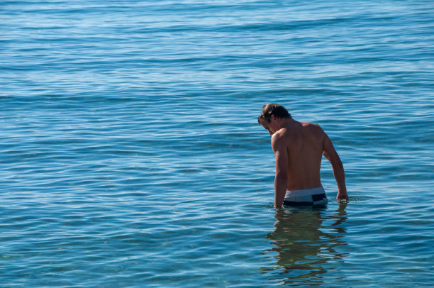 一个年轻人站在地中海的蓝色海水中游泳图片下载