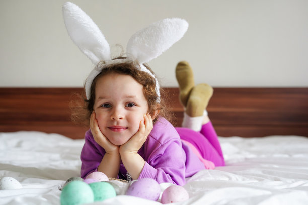 复活节快乐。可爱的漂亮女孩卷发和兔子耳朵躺在床上与彩色的复活节彩蛋。生活的照片图片下载