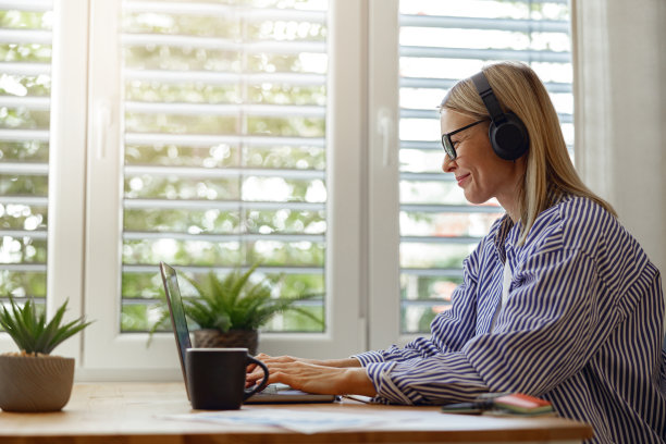 微笑的女程序员戴着耳机在家里办公室的笔记本电脑上在线工作图片下载