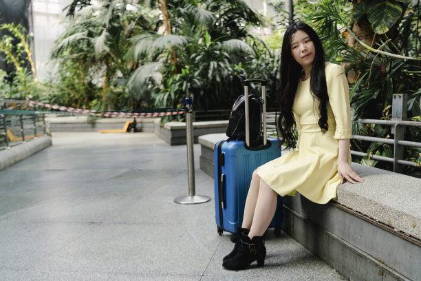 一个穿着黄色衣服、提着蓝色行李箱的女孩在车站等候交通工具图片下载
