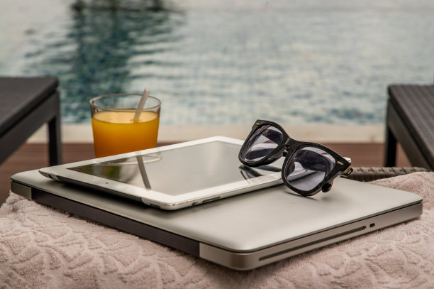在泳池边放松的时刻。从笔记本电脑和平板电脑上休息一下，享受新鲜的橙汁。图片下载