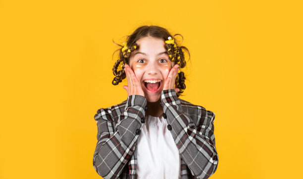 带着眼罩的快乐孩子。小女孩用卷发器把头发卷起来。创造美丽的发型。理发师沙龙。女孩与卷发器和发夹在她的头发在黄色背景。美丽的发型图片下载