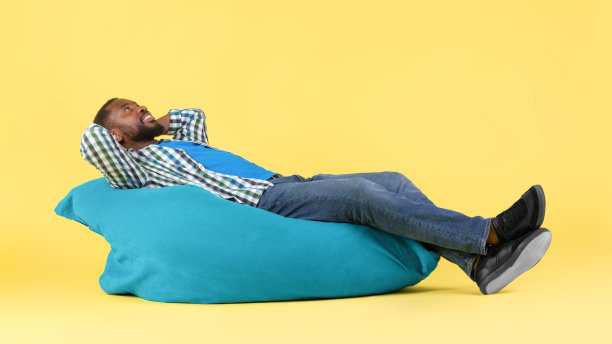 一个黑人躺在豆袋椅上，在黄色的背景下放松图片下载