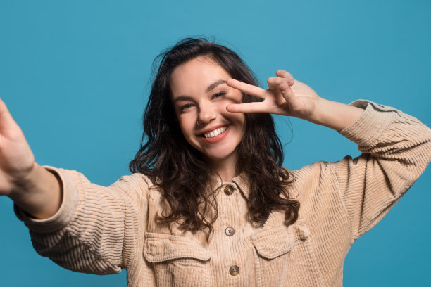 快乐的千禧欧洲黑发女性在随意自拍和和平标志图片下载