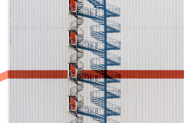 一个现代仓库上带有强烈阴影的红色螺旋逃生楼梯的详细视图图片下载