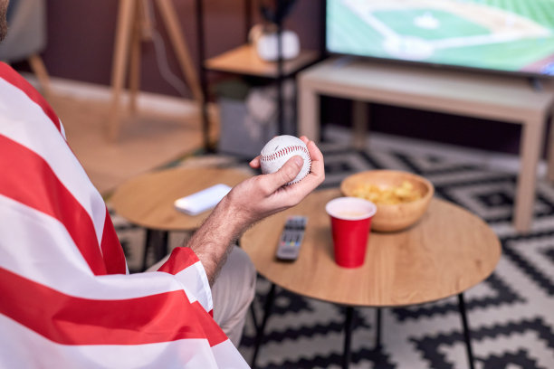 在电视上观看比赛时，体育迷手持棒球的特写镜头图片下载