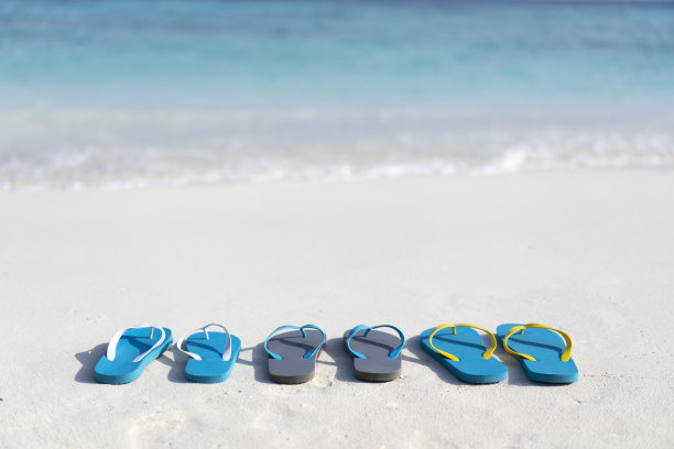 马尔代夫海滩上的三双人字拖，背景是海洋。家庭度假图片下载