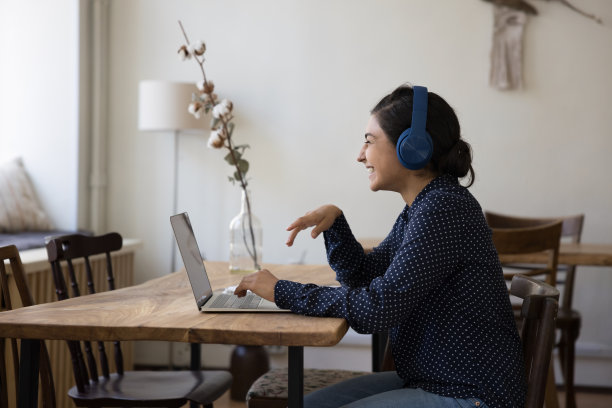 快乐的成年印度学生女孩戴着耳机对着笔记本电脑笑图片下载