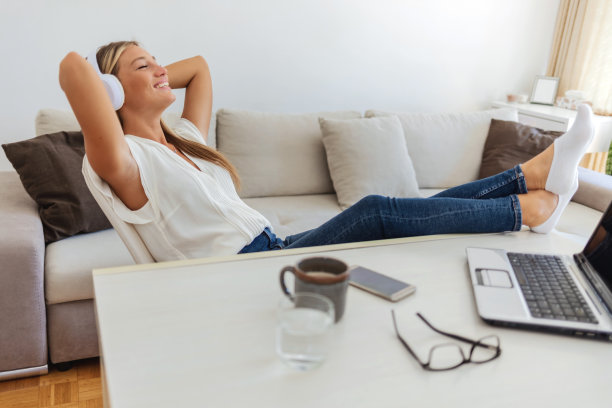 微笑的年轻女子戴着耳机听音乐。年轻女子一边听音乐一边用电脑。图片下载