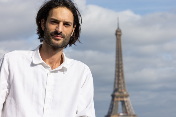 一个英俊的微笑的年轻黑发男子的肖像与埃菲尔铁塔和巴黎的背景图片下载