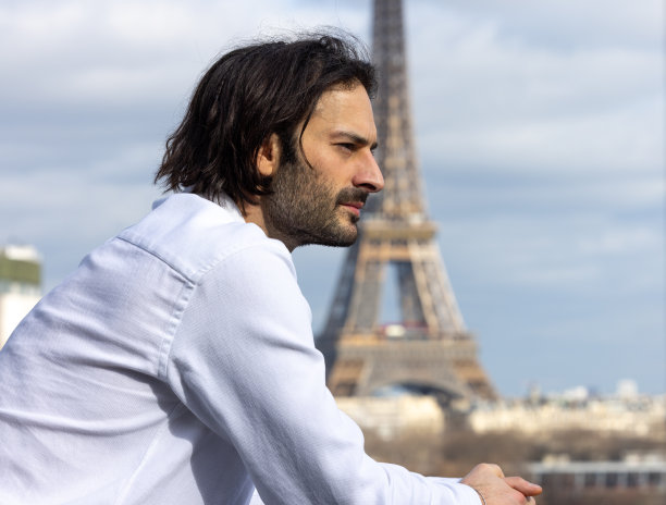 一个英俊的微笑的年轻黑发男子的肖像与埃菲尔铁塔和巴黎的背景图片下载