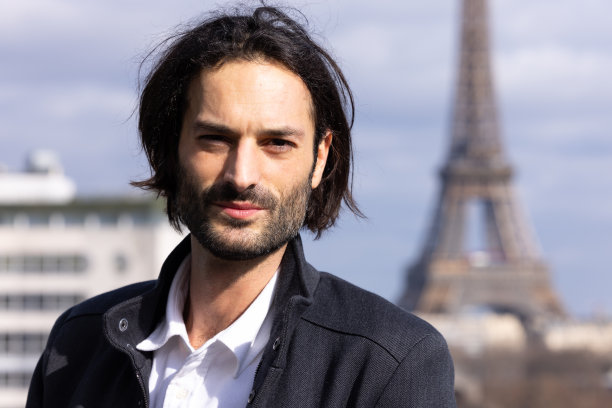 一个英俊的微笑的年轻黑发男子的肖像与埃菲尔铁塔和巴黎的背景图片下载