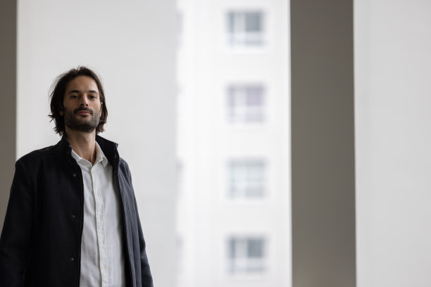 一个时尚的年轻人站在他的公司办公室在一个大飘窗前的肖像图片下载