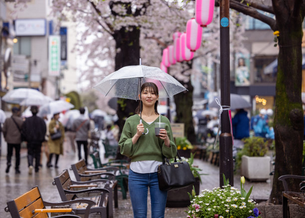 年轻女子站在樱花下在一个雨天的城市图片下载