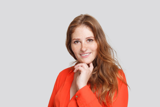 室内肖像迷人的年轻女子姜黄色头发和雀斑的脸摆姿势在白色的工作室墙，穿着红色衬衫图片下载