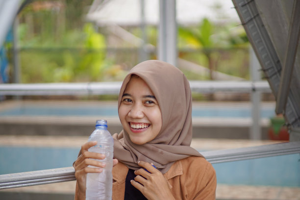 穆斯林亚洲妇女戴着头巾微笑着拿着水瓶图片下载