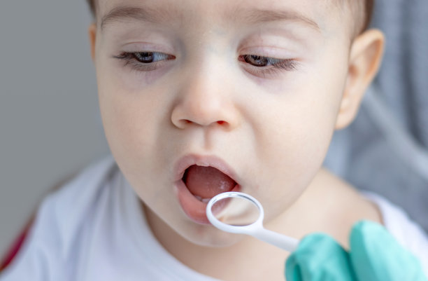 小孩，小孩，婴儿，在牙医柜里，戴着手术手套，用镜子嘴检查牙齿。学龄前男孩在粉红色浴袍上用电动牙刷清洁图片下载