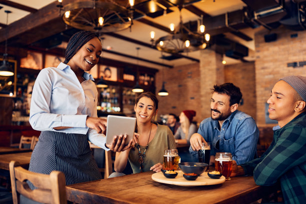 在酒吧里，快乐的黑人女服务员使用触控板从菜单上建议她的顾客点单。图片下载