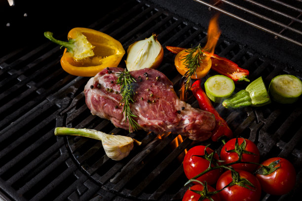 在闷烧的炭火上烤生猪肉，配迷迭香、大蒜、洋葱、胡椒粉、西葫芦、西红柿。水平方向图片下载