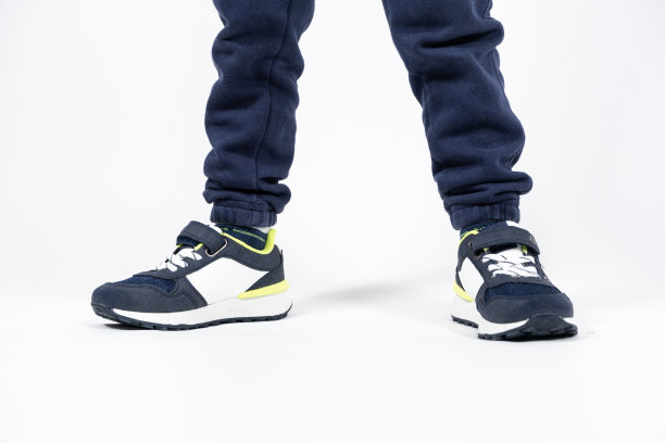 儿童鞋。蓝色的孩子跑鞋，运动鞋上的腿上是一个五、六岁男孩的白色背景。图片下载